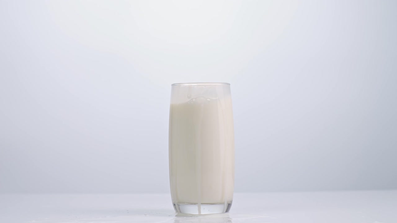 cubos de hielo cayendo en un vaso de leche sobre un fondo blanco