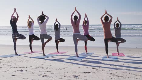 grupo multiétnico de mujeres haciendo posición de yoga en la playa y fondo de cielo azul