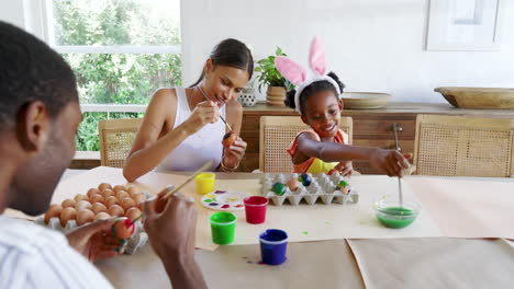diverse family painting easter eggs together, smiling and enjoying creative time at home