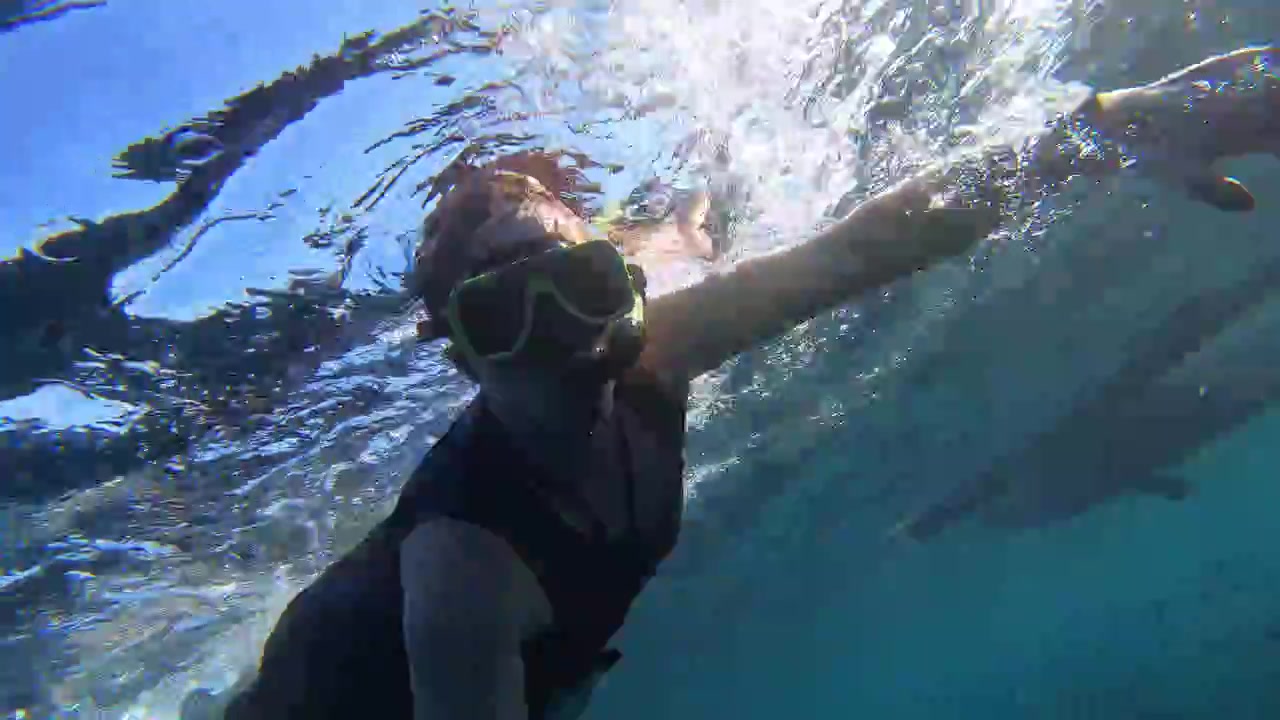 Um homem filmando a si mesmo enquanto mergulha com snorkel, mostrando a vista subaquática de um enorme cardume de sardinhas.