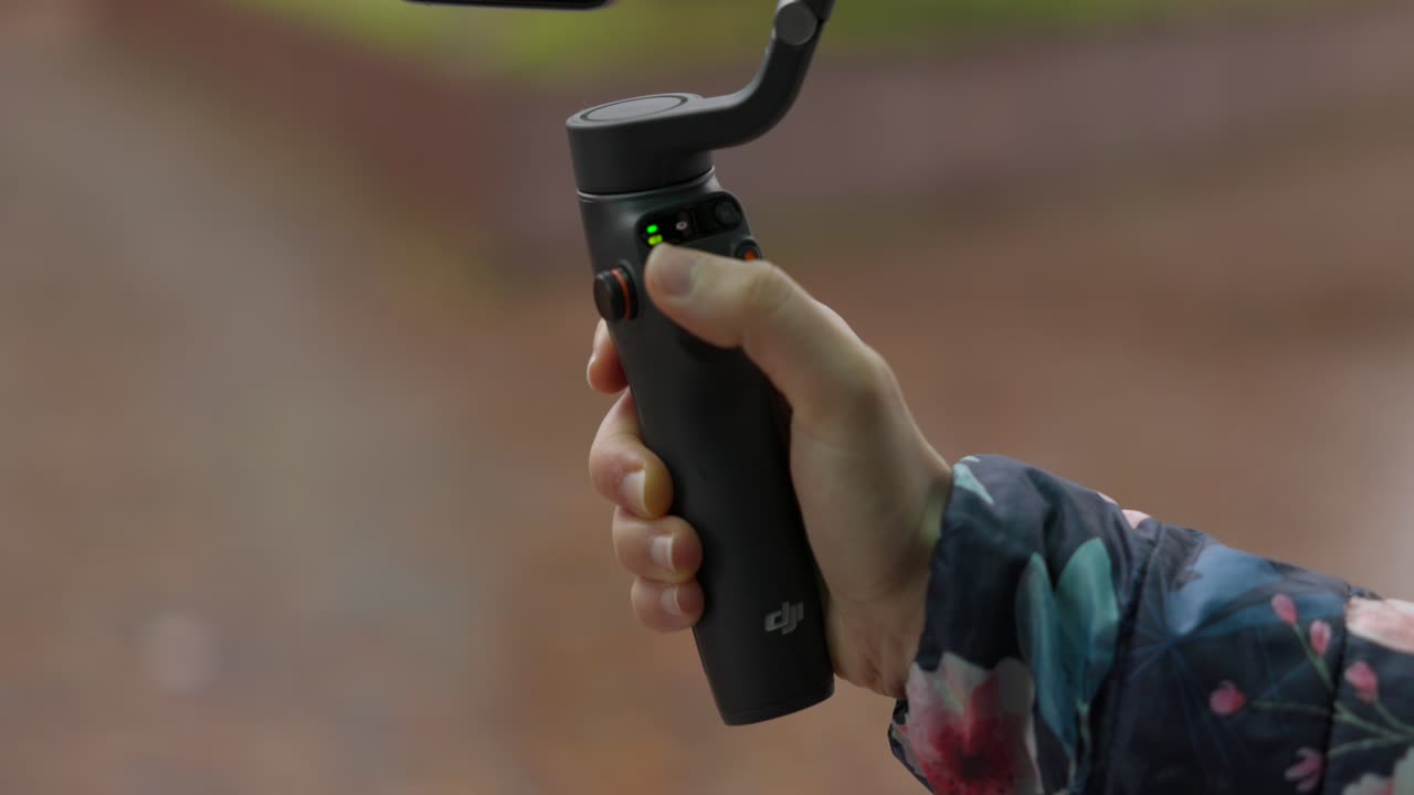 여성 손은 dji osmo mobile 6 gimbal를 잡고 엄지 손가락으로 버튼을 누릅니다.