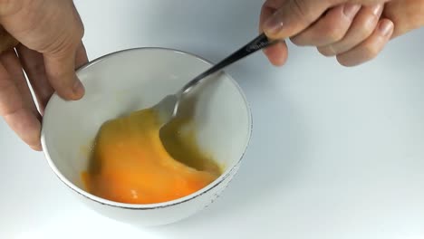 batiendo un huevo en un cuenco de cerámica blanca con un tenedor, todavía, aislado, slomo