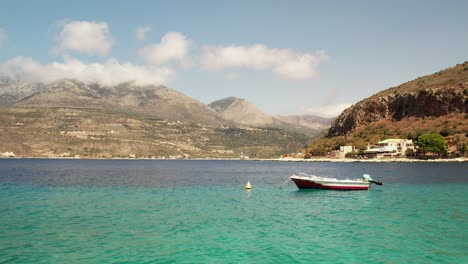 El-Movimiento-Aéreo-De-Paralaje-Cerca-Del-Nivel-Del-Mar-Revela-Pequeños-Barcos-De-Pesca-Mientras-La-Cámara-Gana-Altitud-En-Un-Día-De-Verano-Con-Pocas-Nubes-En-El-Fondo-Que-Cubren-La-Ladera-De-La-Montaña