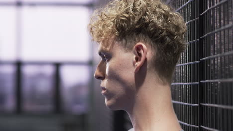 young man with curly hair smiling confidently at indoor padel tennis indoor court, copy space