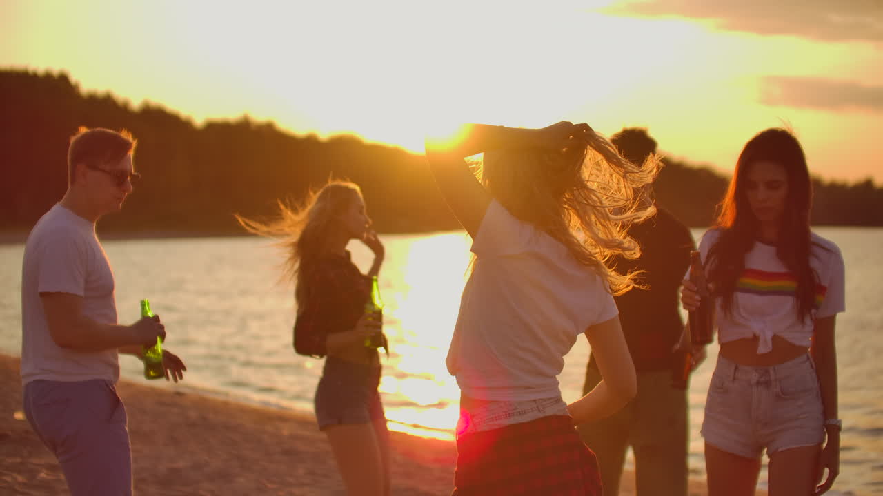 The young people dance in circles on the open air party with beer. It is crazy and cool beach party with the best friends in the good mood.