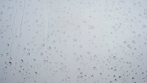 a slow-motion footage of a close-view of heavy rain drops is seen through a window glass