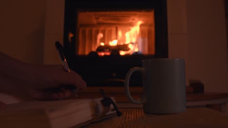 cozy background of a young female hand writing on a old notebook near a warm fireplace, with a cup with hot steam getting out of it