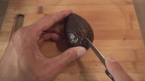 hombre cortando un aguacate maduro por la mitad con un cuchillo de frutas