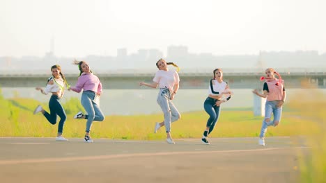 girls in jeans and sweatshirts simultaneously dance street dancing on the road. fashionable women with bright pigtails dance hip-hop in the summer.