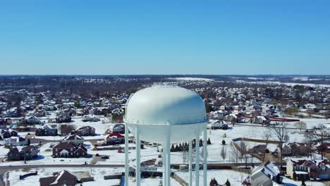 Schwindelaufnahme-Eines-Wasserturms-Mit-Einer-Schneebedeckten-Nachbarschaft-Im-Hintergrund