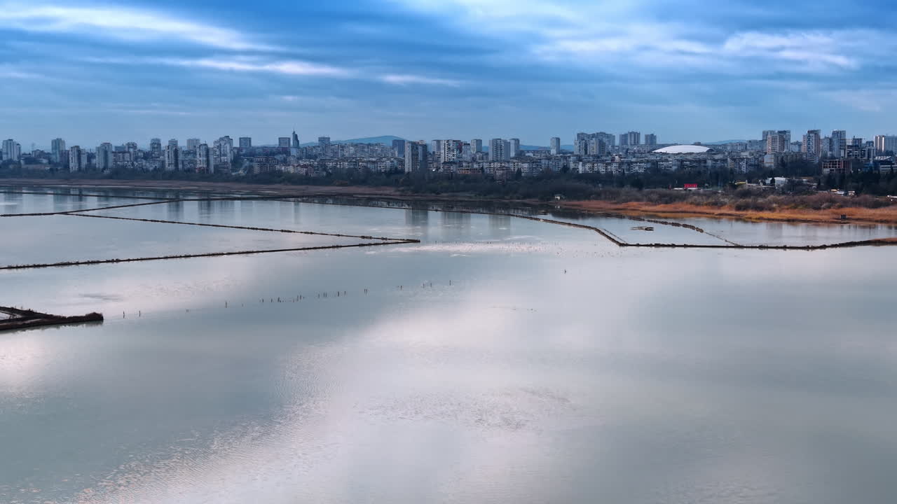 Ampia veduta delle saline con skyline della città sullo sfondo. Bacini idrici industriali per la produzione di sale situati vicino a una moderna area residenziale urbana