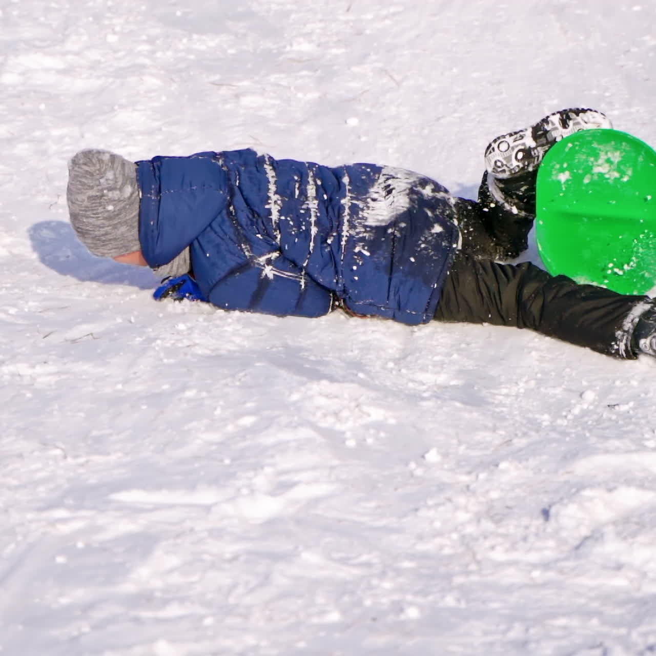 Boy sledding on a snow hill. Child riding down the slide on a plastic sled in winter. Happy childhood. Slow motion.
