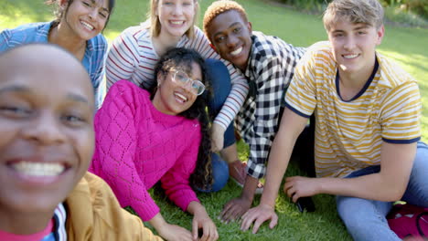 Fröhliche,-Vielfältige-Gruppe-Von-Teenager-Freunden,-Die-Auf-Gras-Sitzen-Und-Sich-Im-Sonnigen-Park-Umarmen,-Zeitlupe