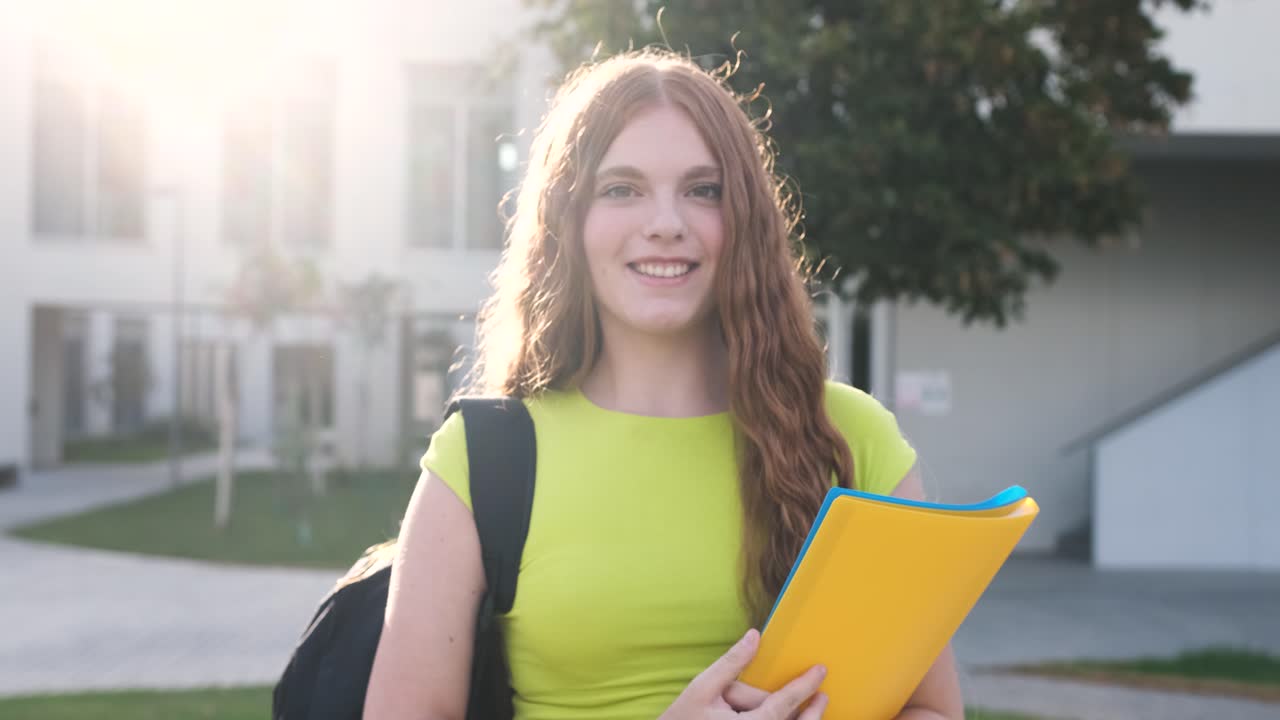 Smiling young female student holding book on university campus