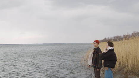 un adolescent et une adolescente debout près du bord de mer par temps nuageux, un garçon montre quelque chose avec son bras