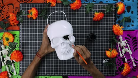 hands painting white skull with vibrant flowers for day of the dead, top view, crafting concept