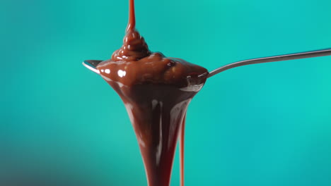 close up of melted chocolate being poured onto spoon and overflowing against blue coloured background with copy space