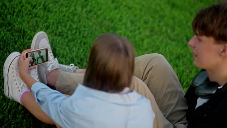 young couple sitting on grass, looking at phone and smiling