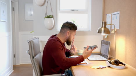 working from home, man using smartphone and laptop at desk in home office