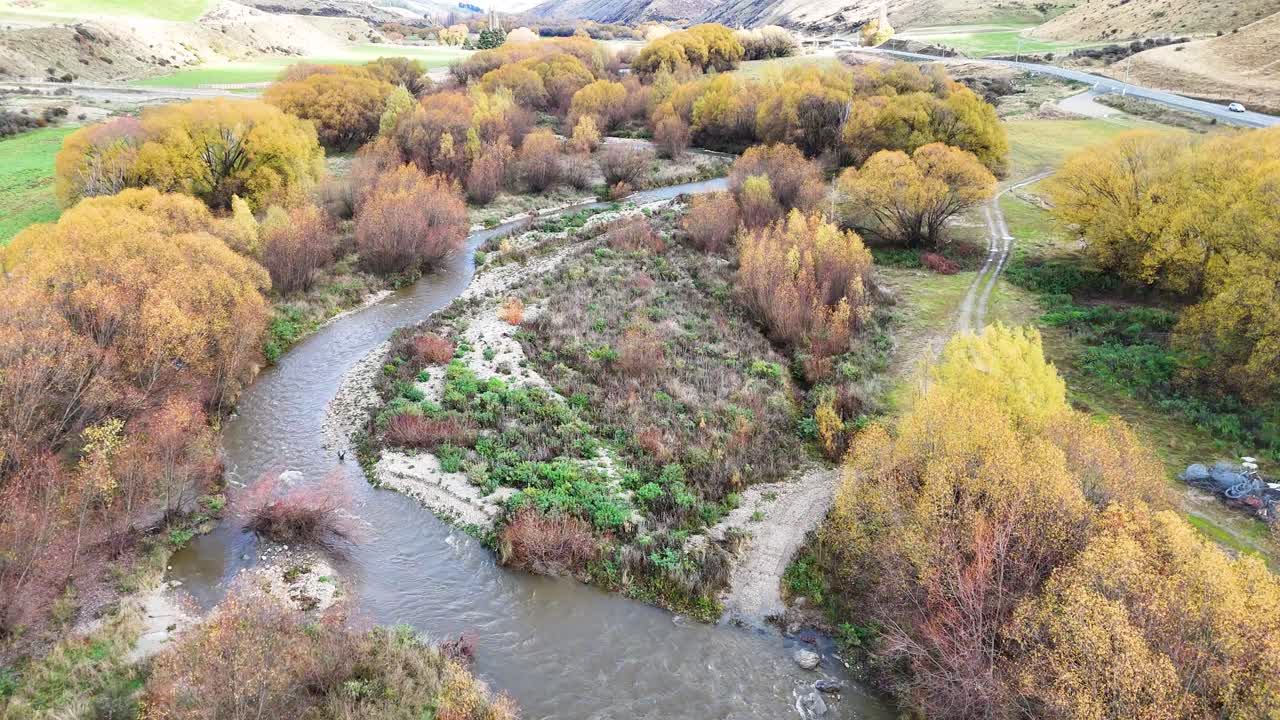 Aerial footage captures a tranquil river winding through vibrant autumn foliage under soft, natural lighting