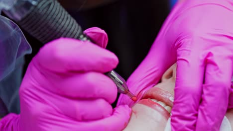 lips tattoo. cosmetologist in pink gloves applying permanent makeup tattoo on lips. modern cosmetology in beauty spa. close-up.