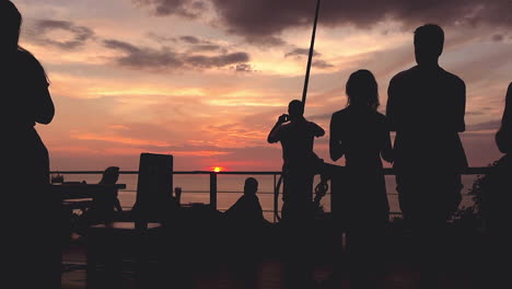 fondo con siluetas de personas de pie en el balcón en el restaurante y viendo el atardecer colorido