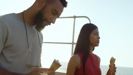 pareja de raza mixta caminando con conos de helado en el paseo marítimo 4k