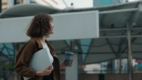 businesswoman walking with laptop and coffee in city