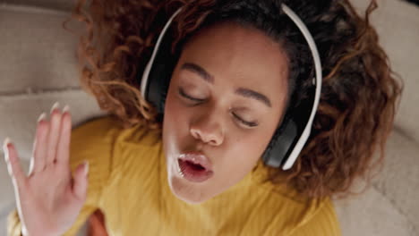 a young woman with curly hair wearing headphones and smiling while lying on a couch, enjoying music.