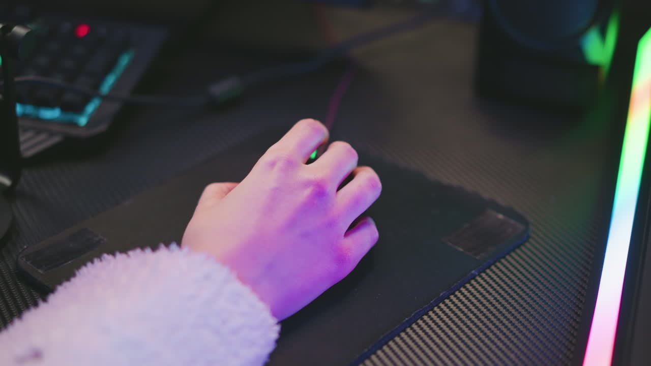 Close up of woman wearing fluffy sweater using computer mouse on black pad in vibrant studio with colorful lighting, focusing on hand movement and digital workspace environment