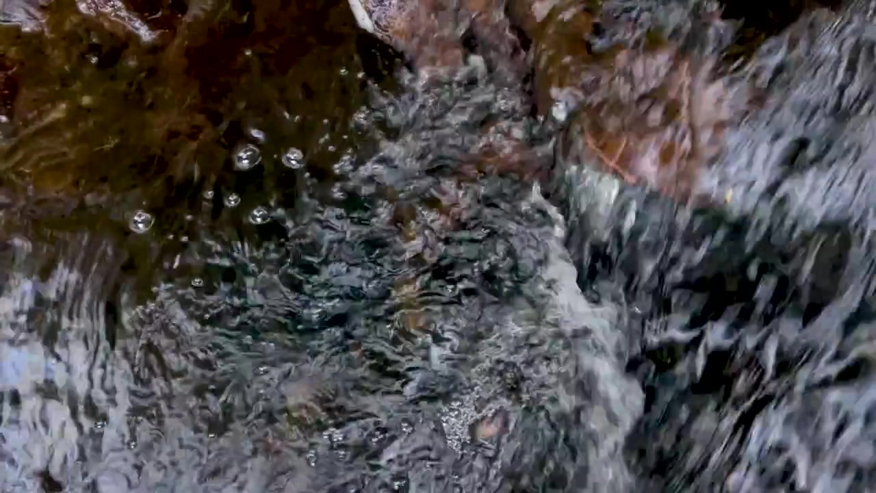 Una vista ravvicinata dall'alto di acqua dolce turbolenta che scorre impetuosamente su pietre e ciottoli scuri e bagnati.