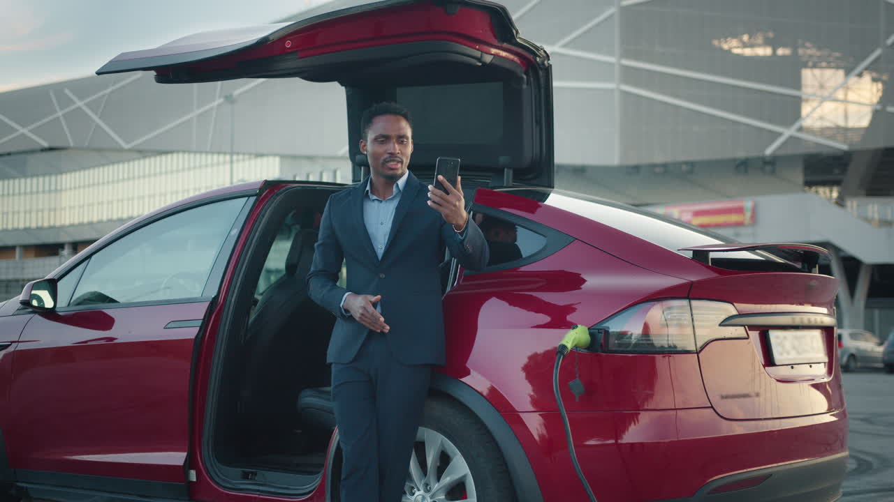 hombre de negocios haciendo una llamada de video cerca de un coche eléctrico