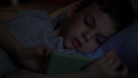 bored preschooler lying on his bed in the dark and used app on his phone.