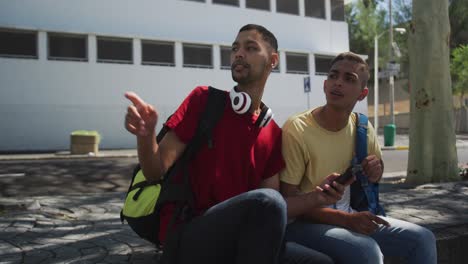 two mixed race friends sitting and using smartphone in the street