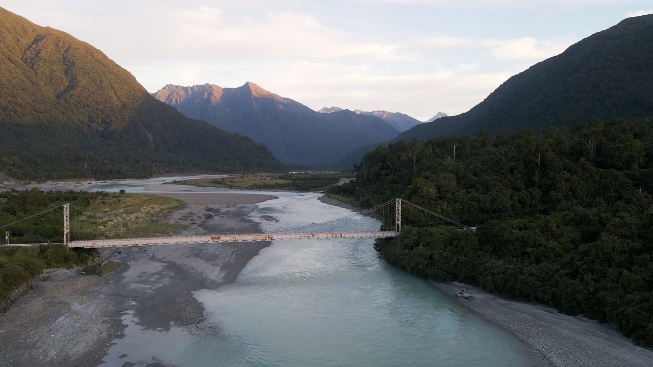 Shallow river coming from rugged mountains and flowing underneath old steel trestle