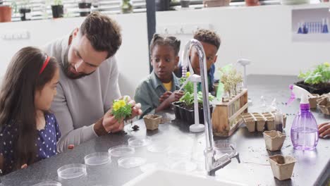 Diverse-male-teacher-and-happy-schoolchildren-studying-plants-in-school-classroom