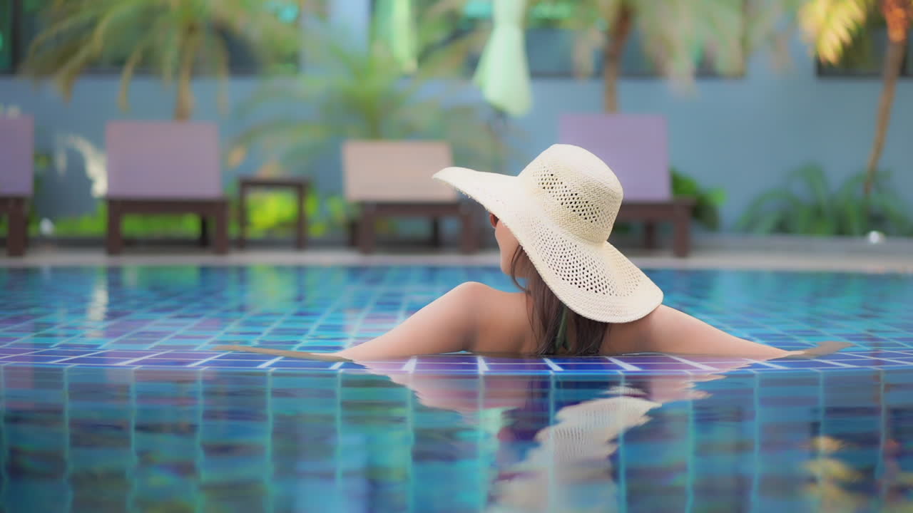 Backside view close-up portrait glamour woman in floppy hat and sunglasses enjoying in swimming pool of exotic hotel spa