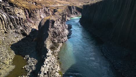 aerial drone forward moving shot over river flowing through studlagil canyon in iceland