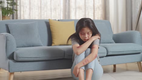 young asian woman victim of violence with bruise on body sitting hugging her knees and crying on the floor at home