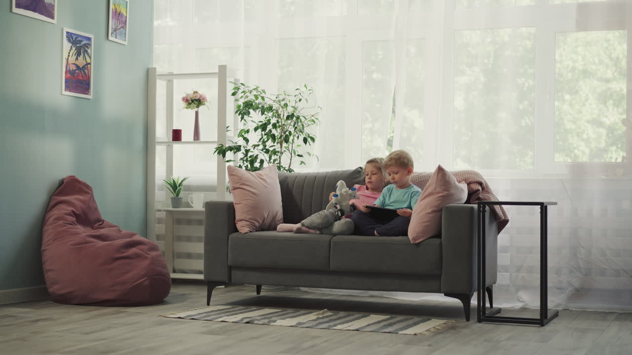 los niños ven dibujos animados educativos en la tableta sentados en el sofá