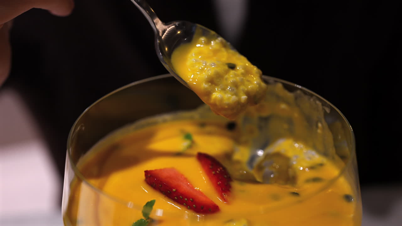 Donna che raccoglie con un cucchiaio un cremoso budino di mango e chia da un'elegante ciotola di vetro con fragole