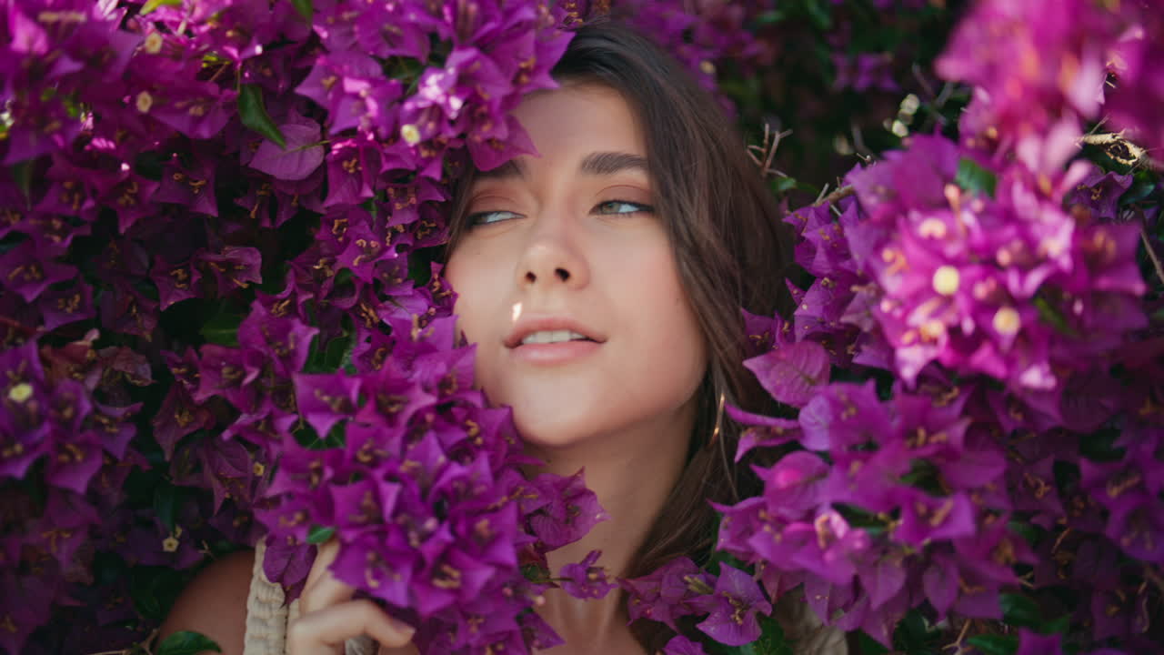 Ritratto di donna sorridente che guarda la fotocamera in un cespuglio di fiori viola. Volto di modella in posa.