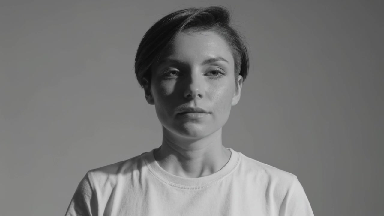 Mulher de camiseta branca em estúdio, fechando e reabrindo os olhos enquanto abaixa o queixo, com a câmera iniciando um teste.