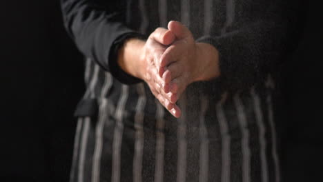 mcu slow motion: male chef wearing apron claps hands together, flour flies through air then rubs hands together