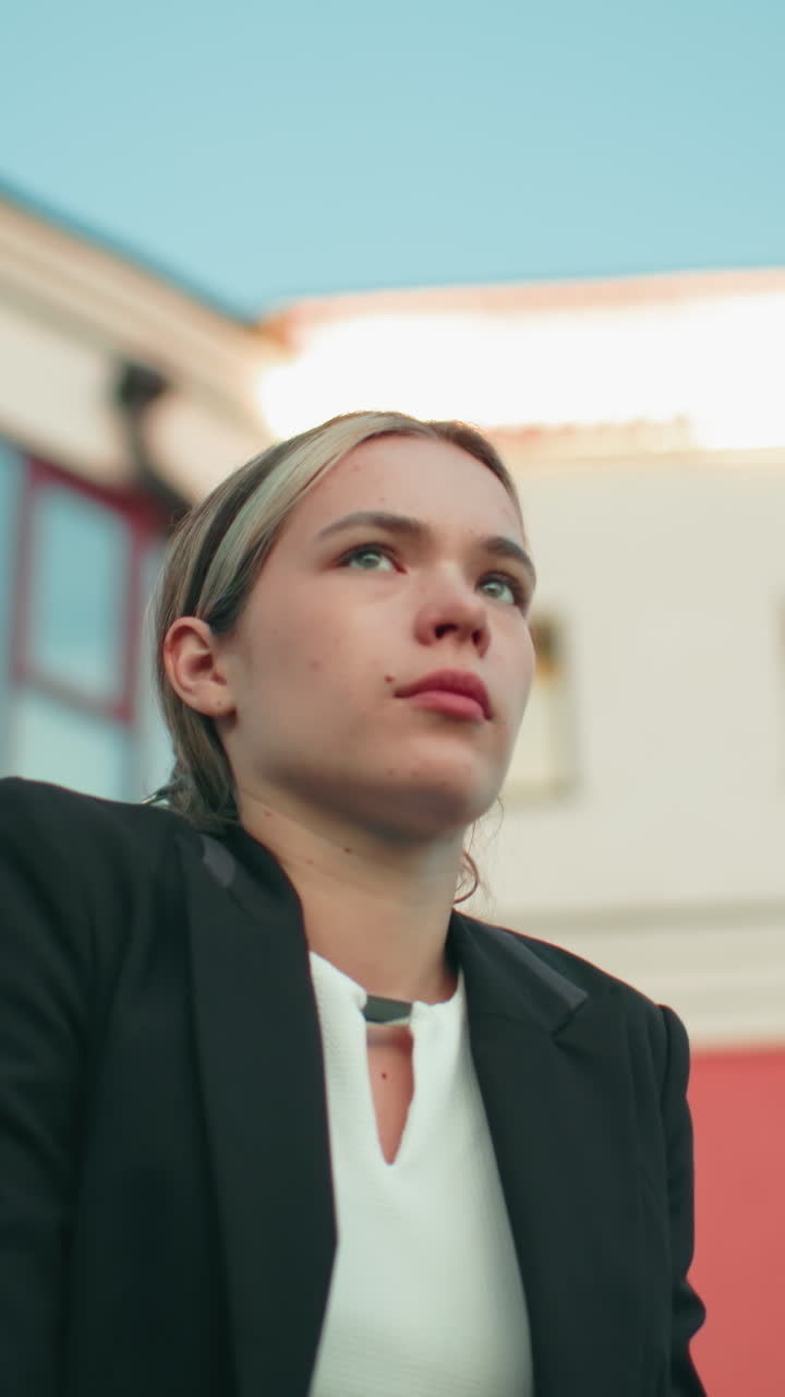 Remote worker in formal outfit leans on iron railing outside residential building, gazing into distance beside lamp post with rooftop light blinking