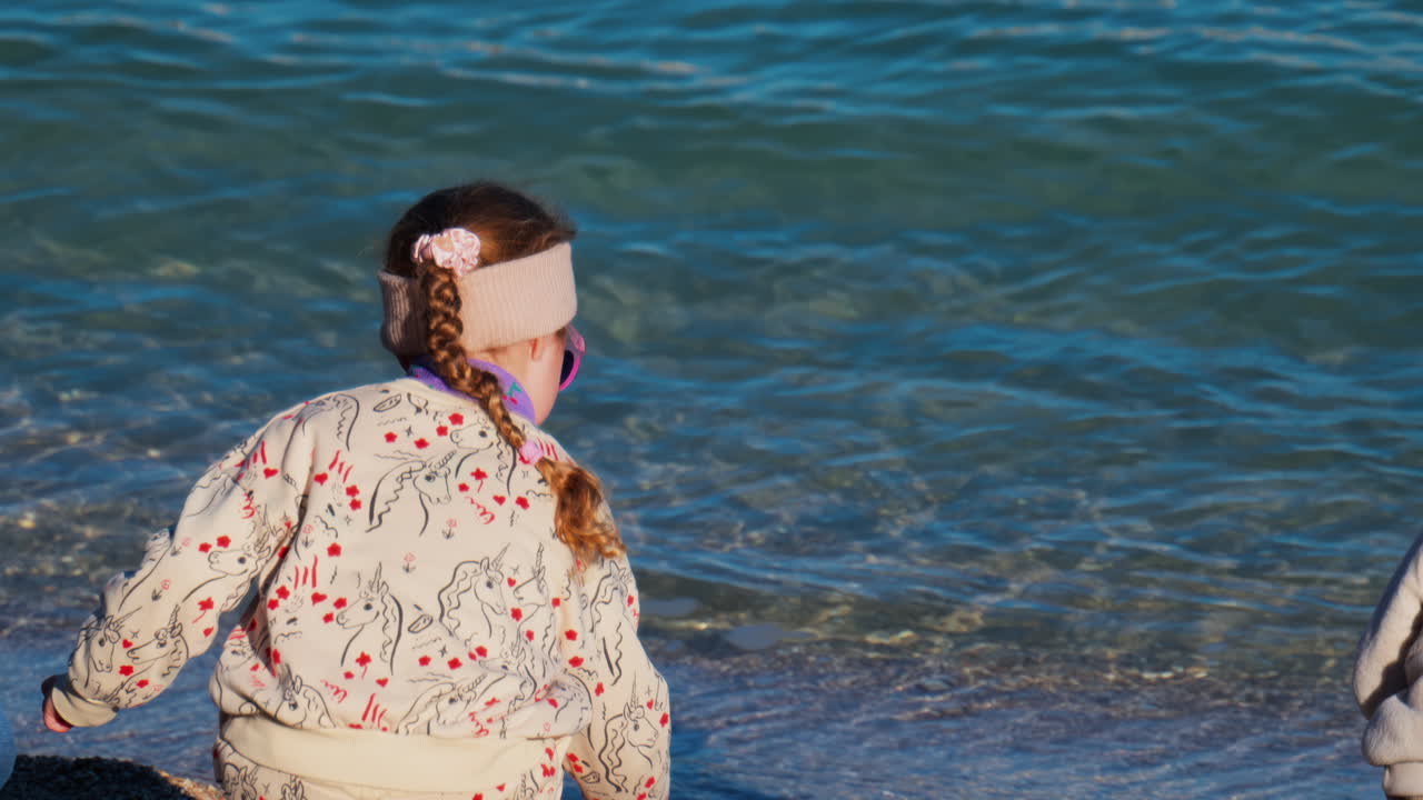 Little girl throwing sand in the sea on the beach