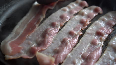 hombre chef cocinando para el desayuno un increíble tocino crujiente, rico en grasa y color, chisporroteando y fumando en una sartén caliente