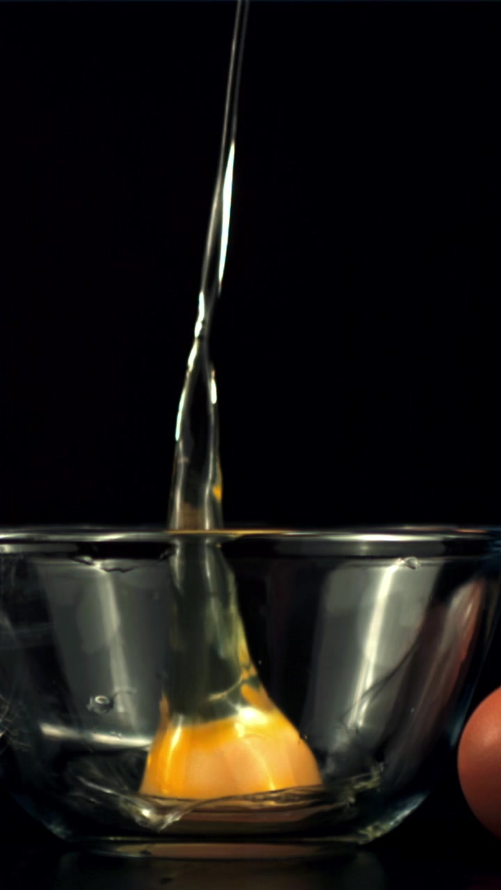 Raw Egg Yolk and White Falling into a Glass Bowl