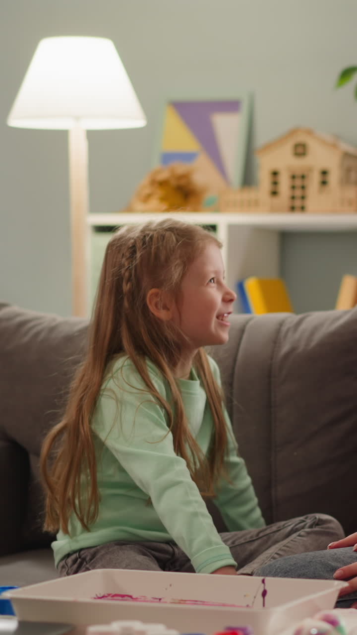 Wondered long haired elder sister discusses with joyful little girl Easter eggs coloring in apartment slow motion. Ebru design technique usage in decor
