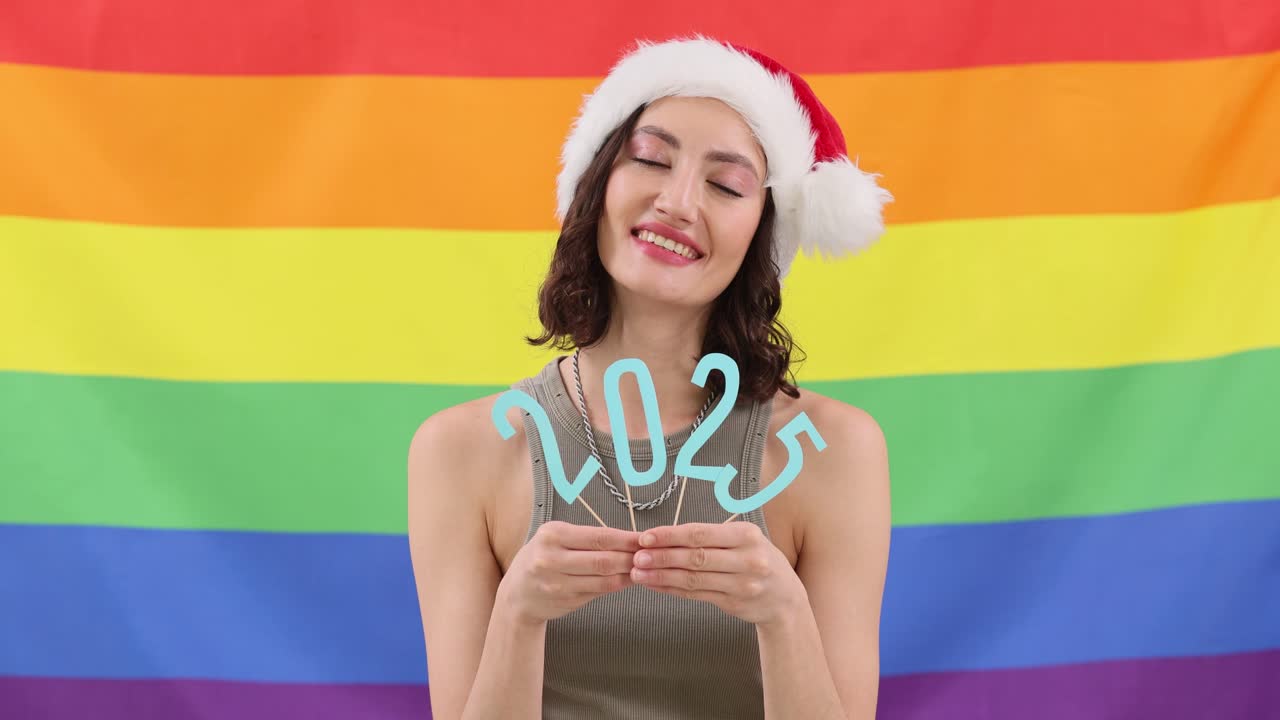 Woman in Santa Hat Holding "2025" Against a Rainbow Flag
